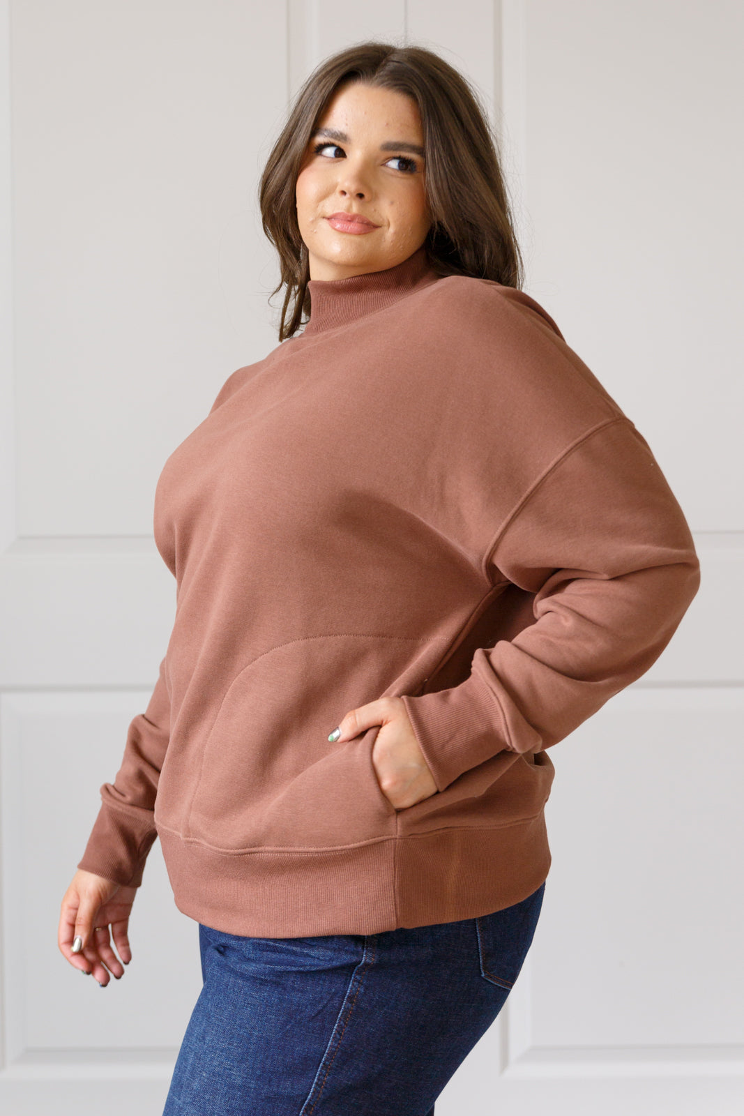 Woman wearing a brown sweatshirt and blue jeans against a white background