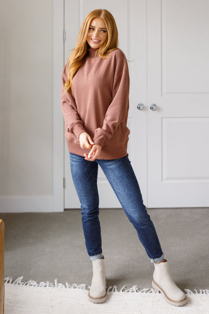 Woman wearing a pink sweater, blue jeans, and white boots standing in a room with a neutral color scheme.