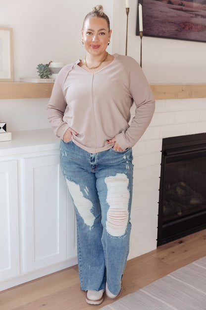 Woman wearing a beige sweater and ripped blue jeans in a living room.