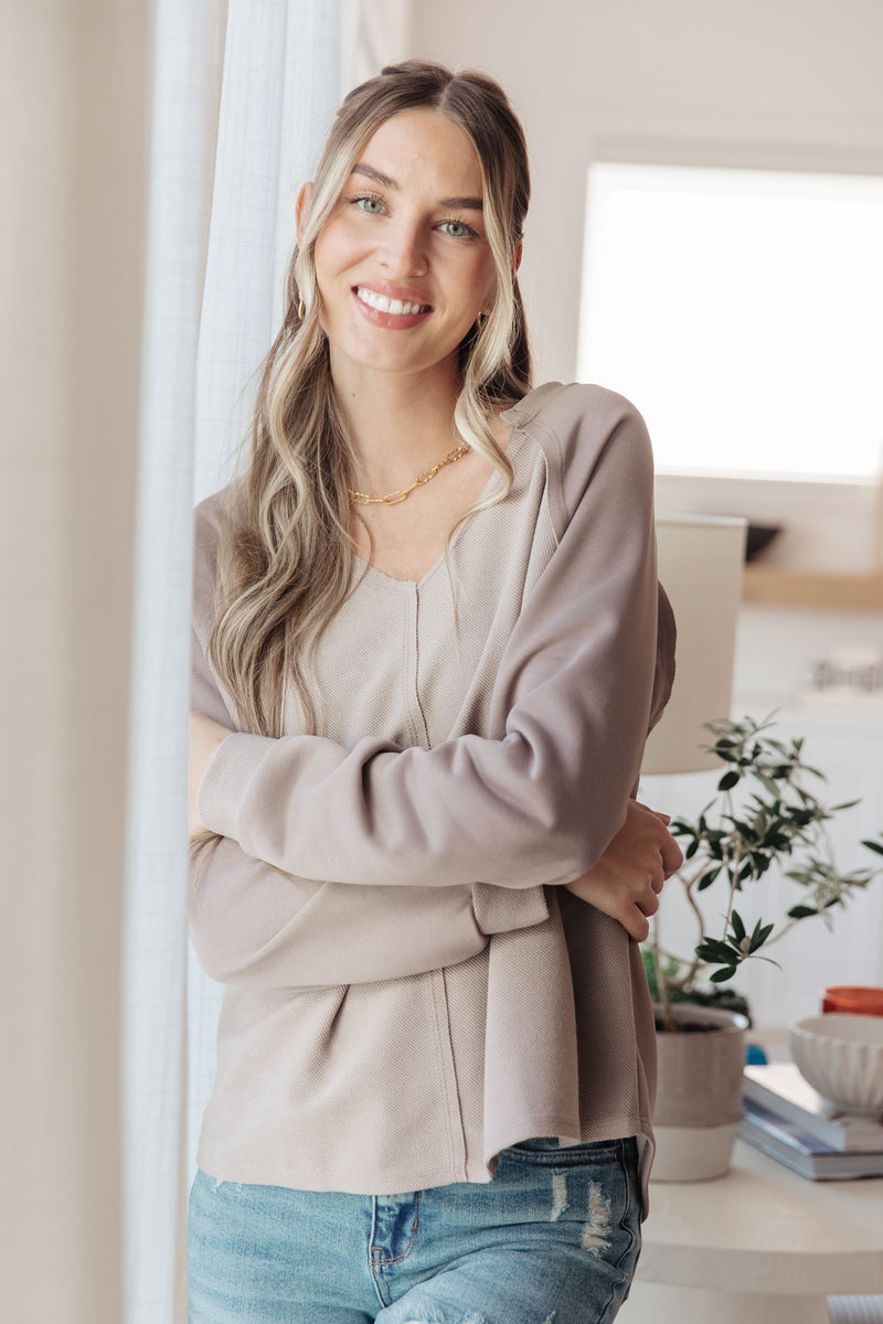Woman standing indoors wearing a light gray cardigan and blue jeans, smiling.
