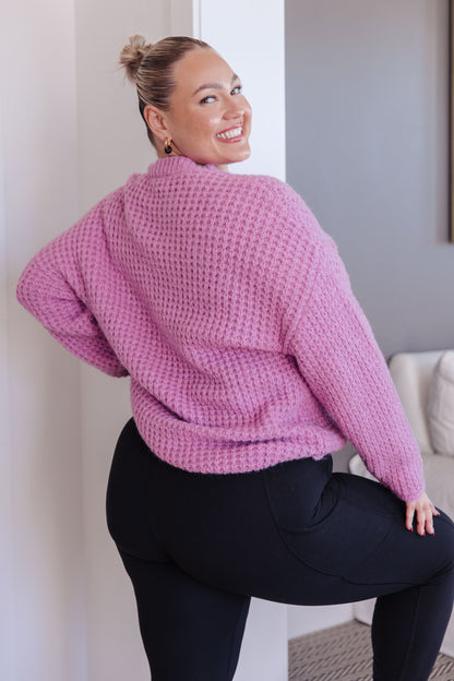 Woman wearing a pink sweater and black pants in a room.