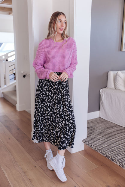 Woman wearing a pink checkered sweater and black floral skirt in a home setting