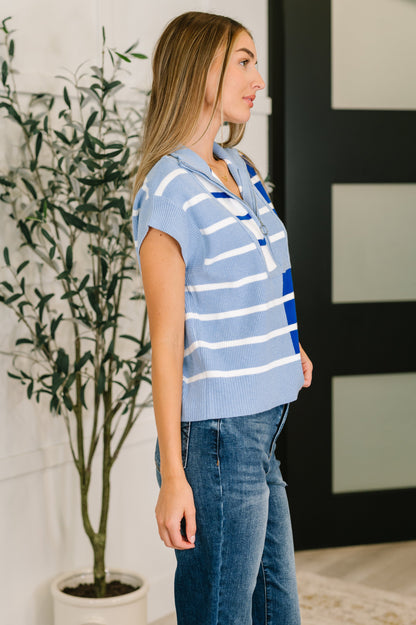 Woman wearing a blue striped shirt and jeans standing indoors with a plant in the background