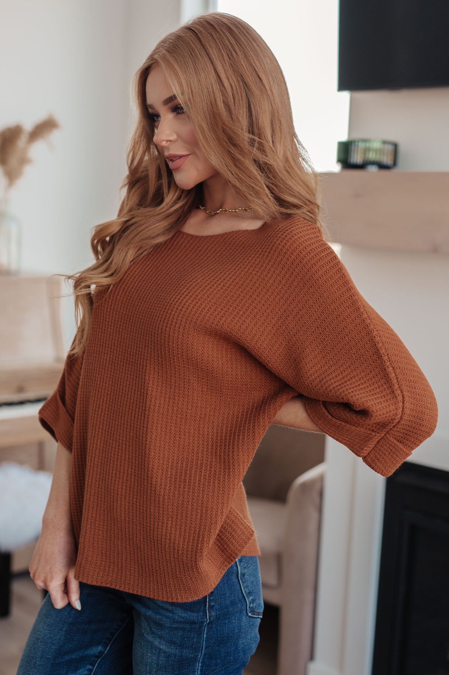 Woman wearing a brown sweater and blue jeans indoors.