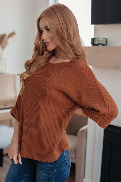 Woman wearing a brown sweater and blue jeans indoors.