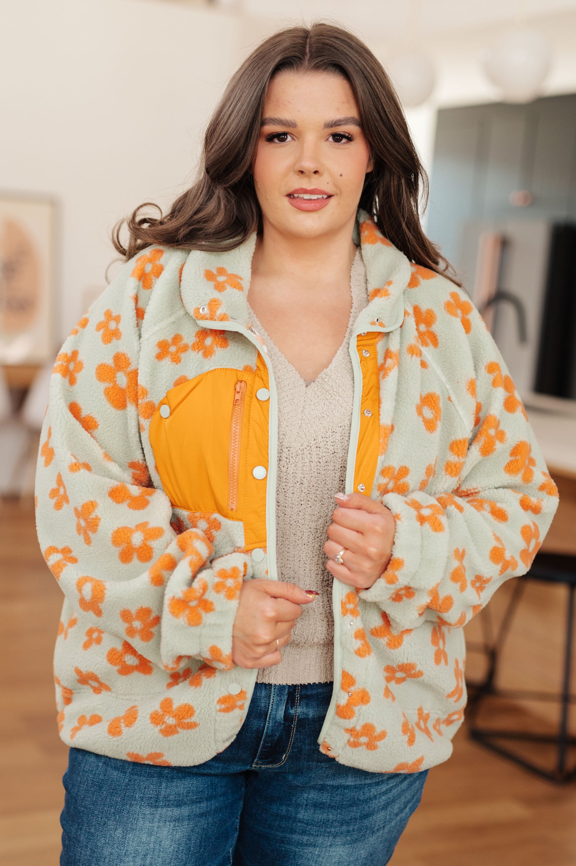 Woman wearing a floral jacket with an orange interior, standing indoors.