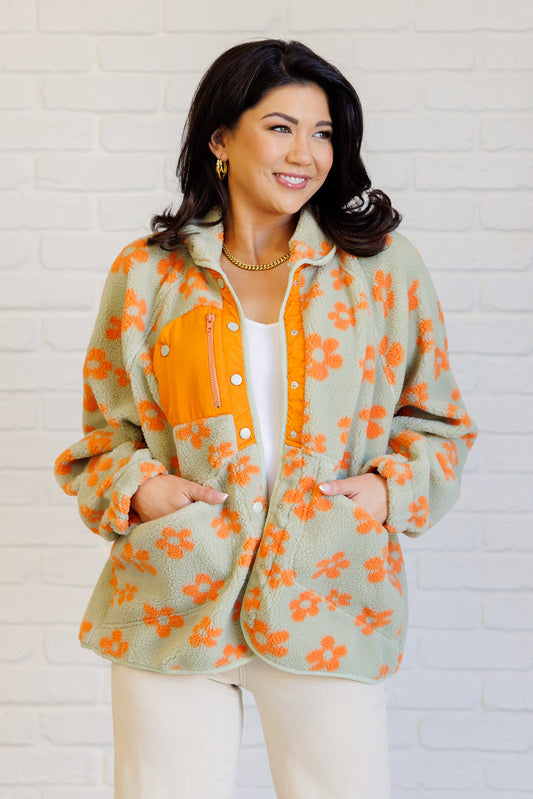 Woman wearing a floral jacket with orange and green pattern against a white brick wall.