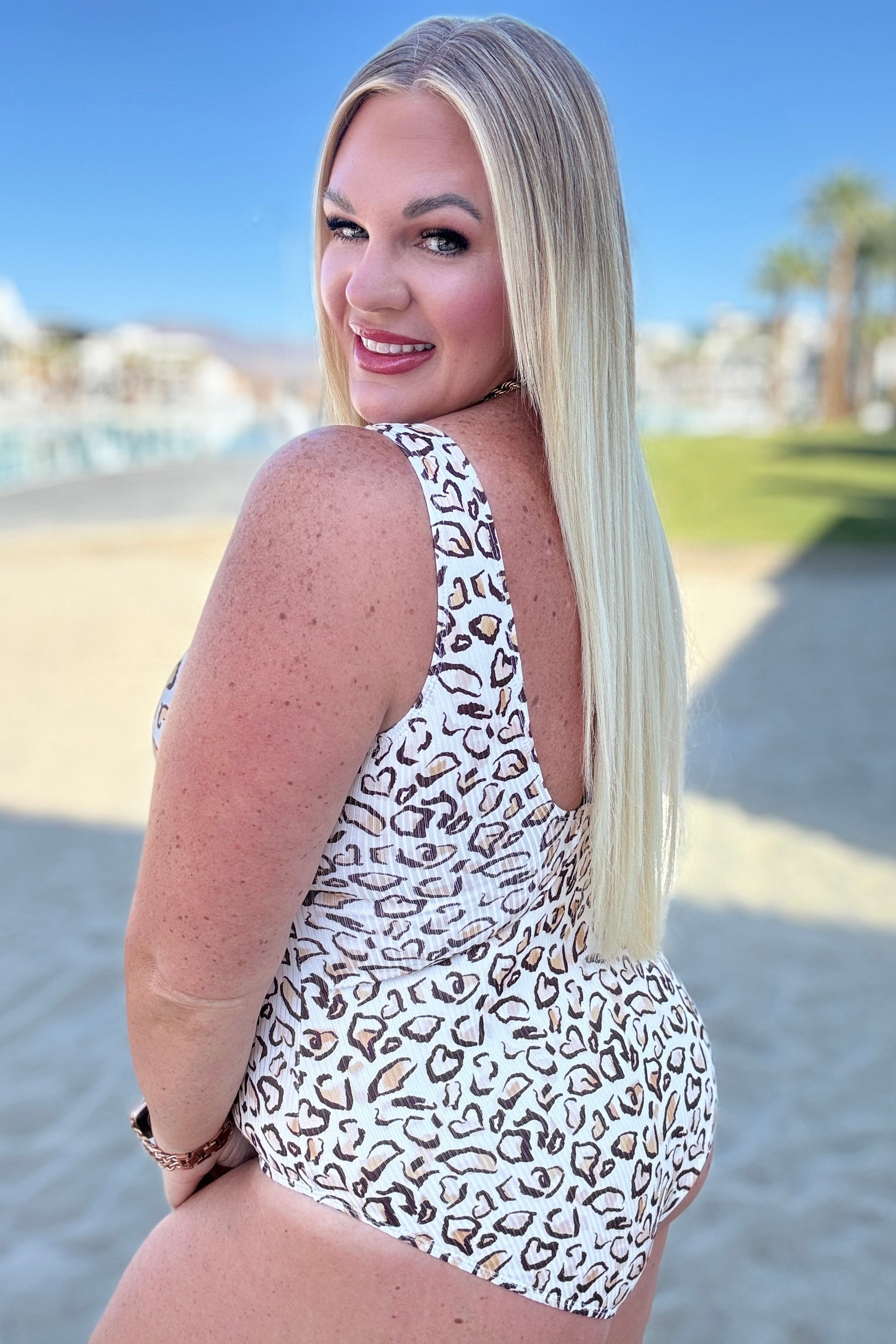 Woman in a leopard print swimsuit standing on a beach with palm trees in the background