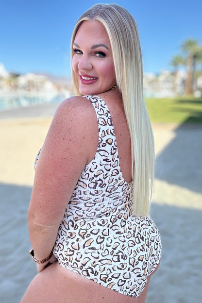 Woman in a leopard print swimsuit standing on a beach with palm trees in the background
