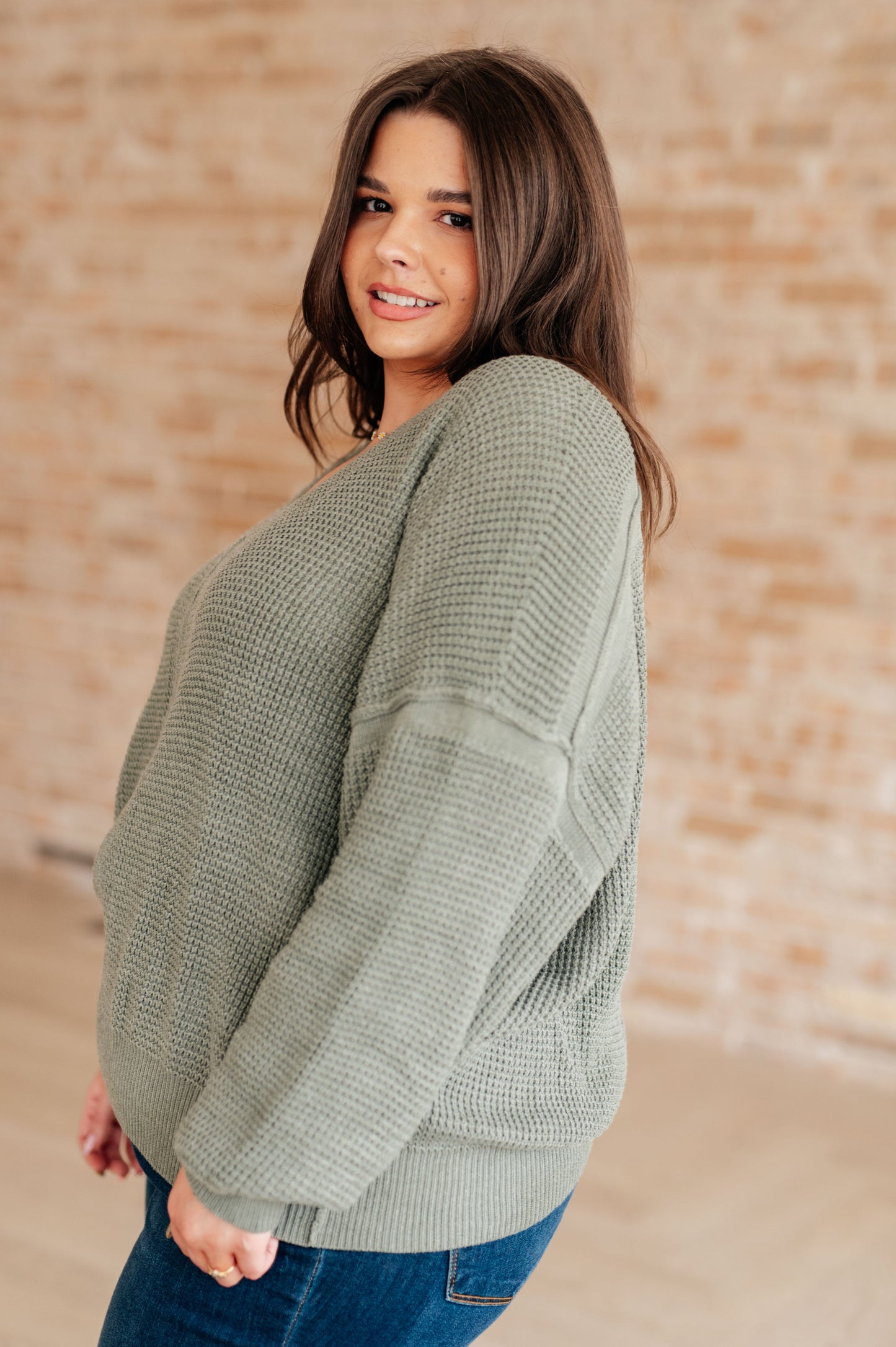 Woman wearing a green sweater against a beige brick wall