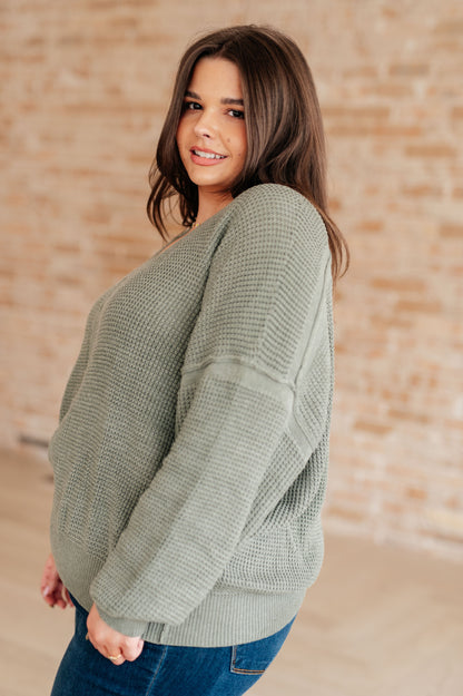 Woman wearing a green sweater against a beige brick wall