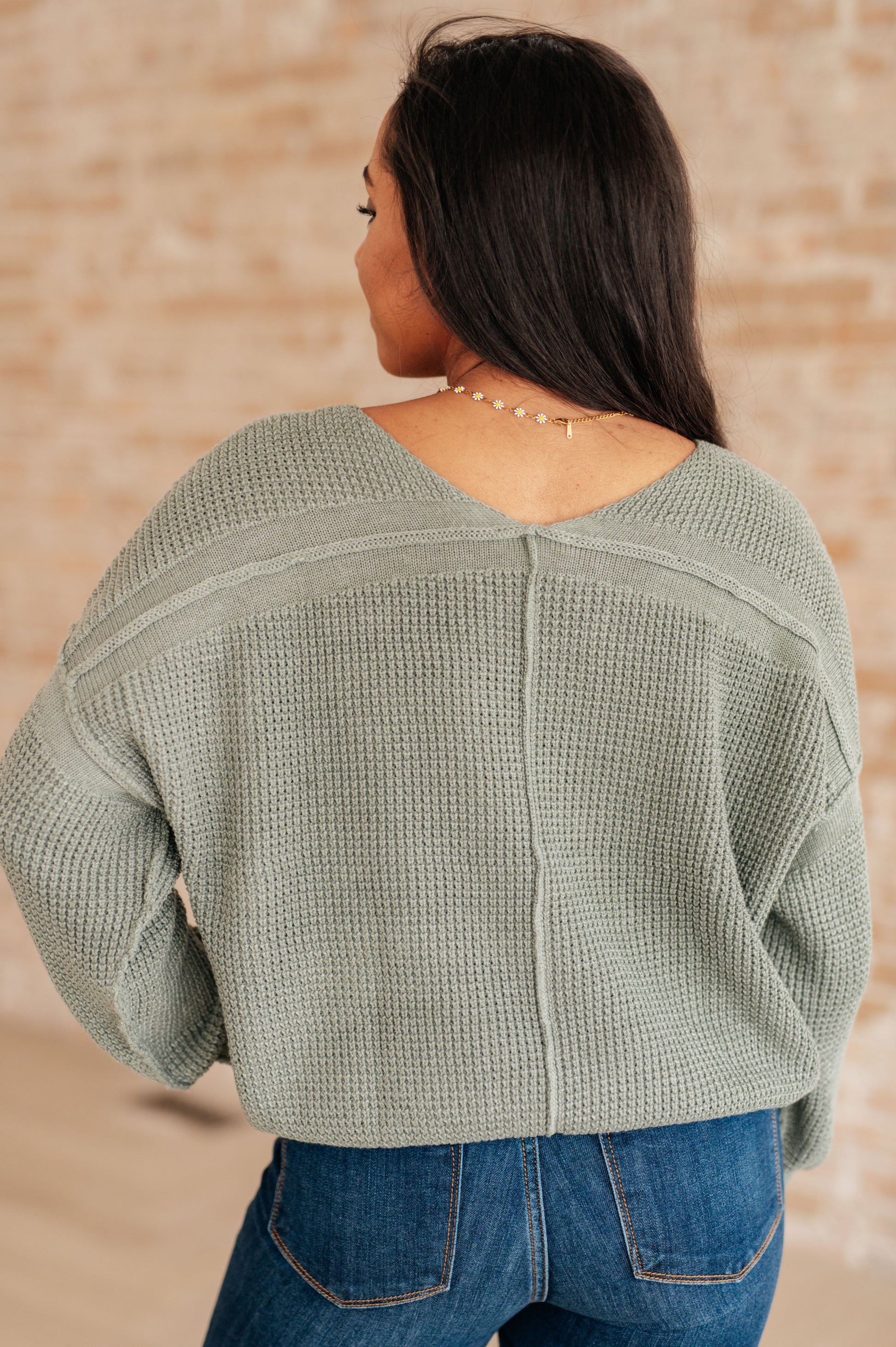 Woman wearing a green textured sweater and blue jeans against a beige wall.