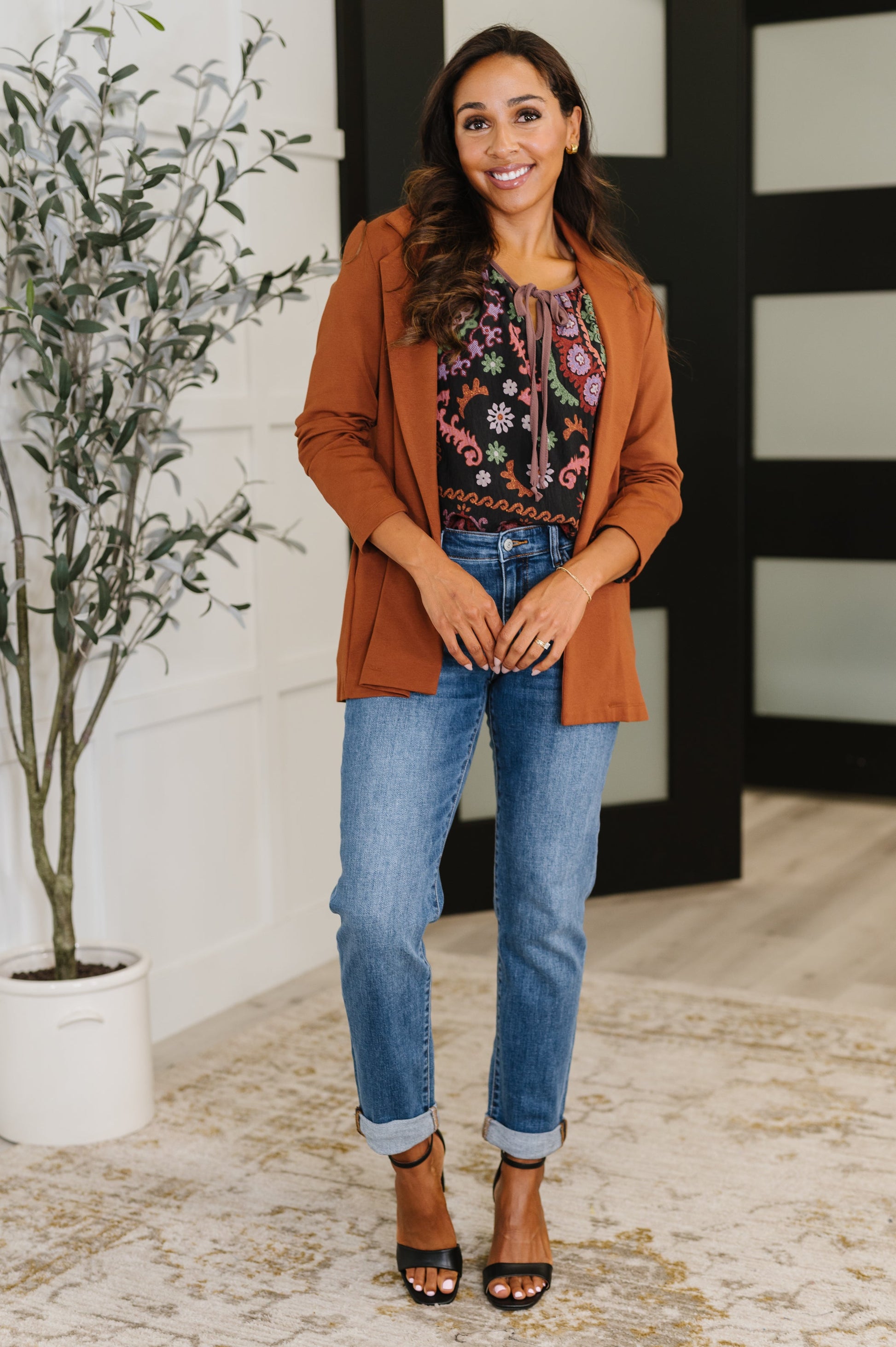 Woman wearing a brown cardigan, floral blouse, and blue jeans indoors.