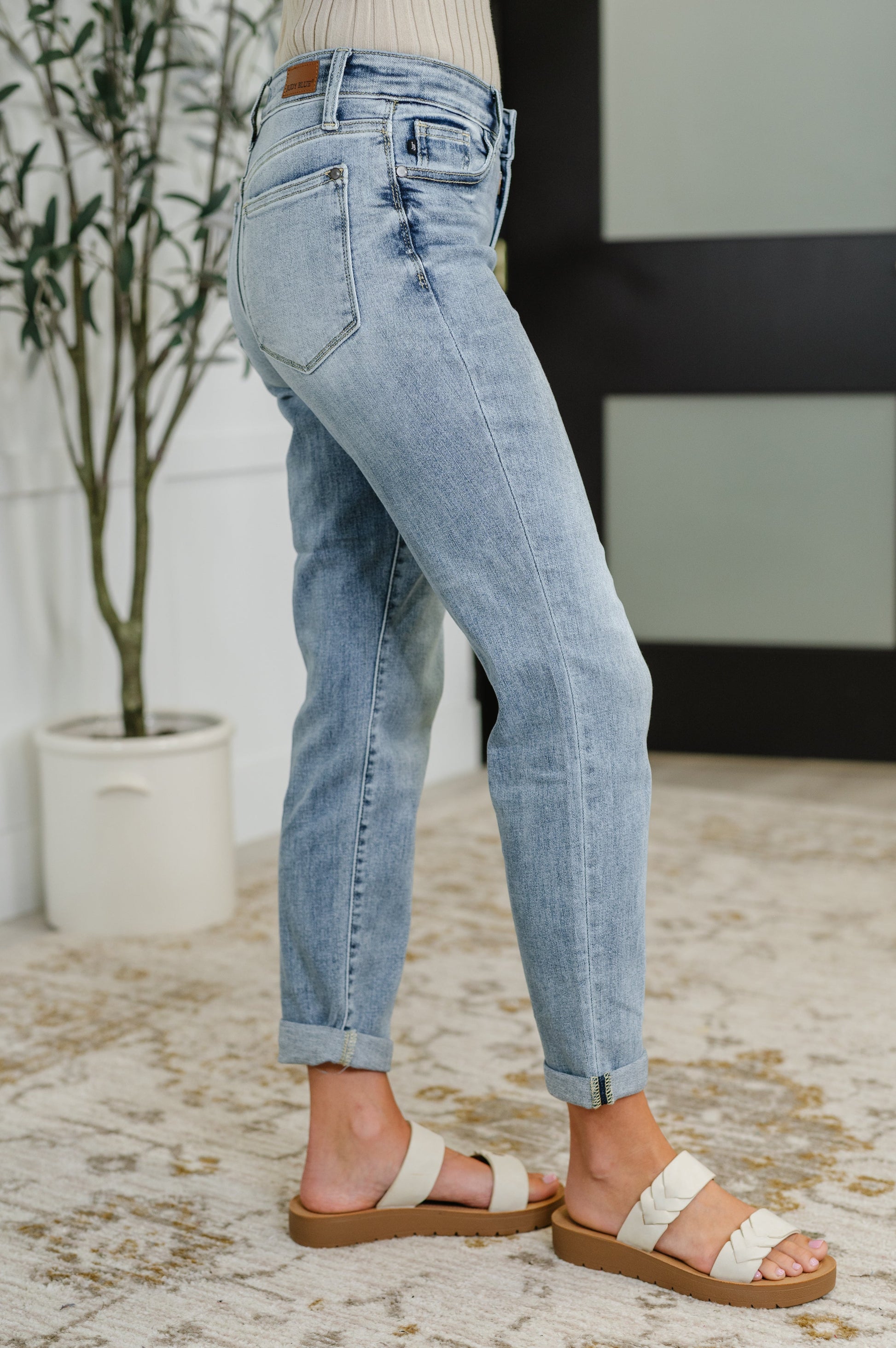 Person wearing light blue jeans and sandals on a neutral background