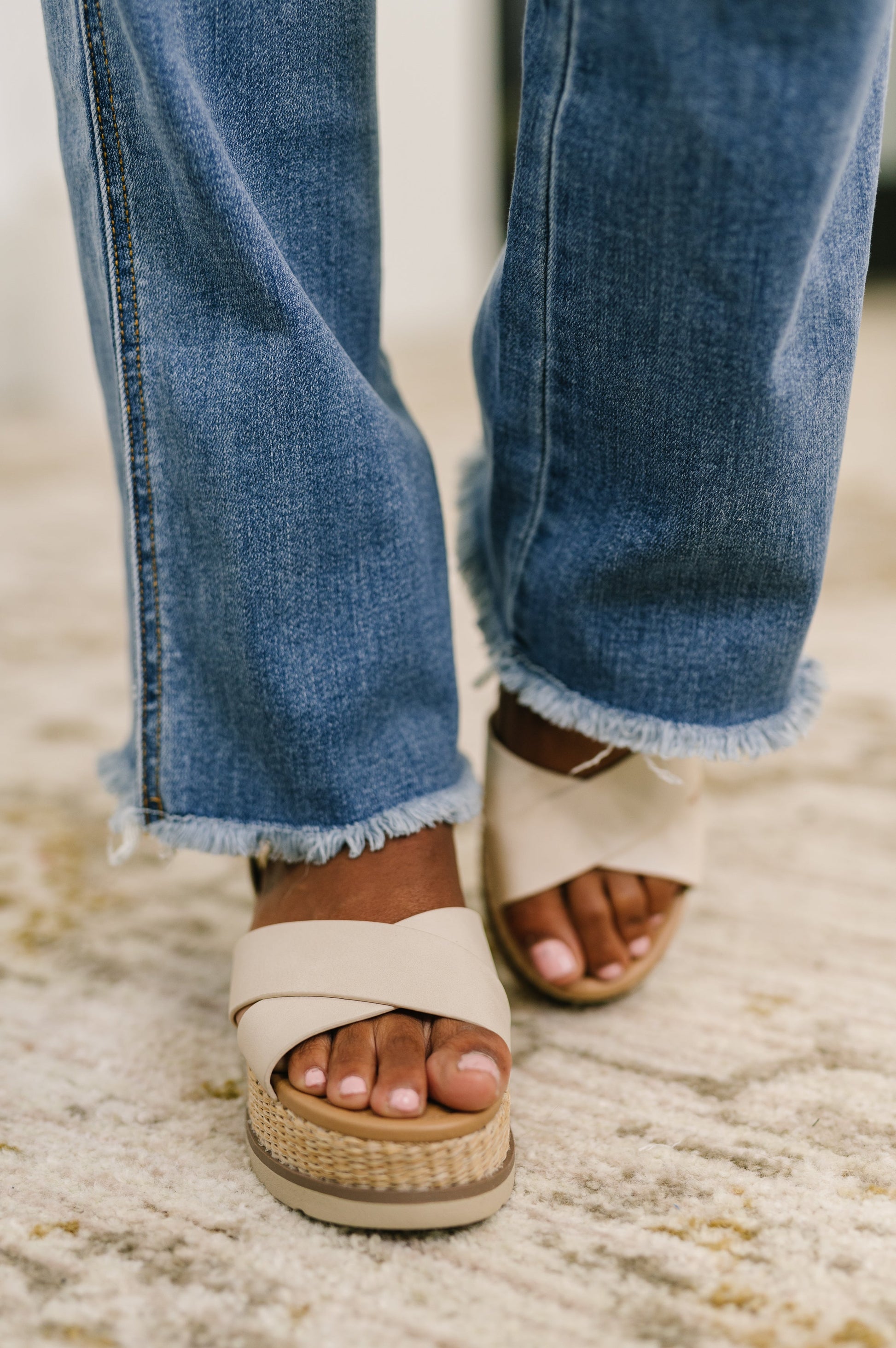 Close-up of blue jeans and beige sandals on a textured surface