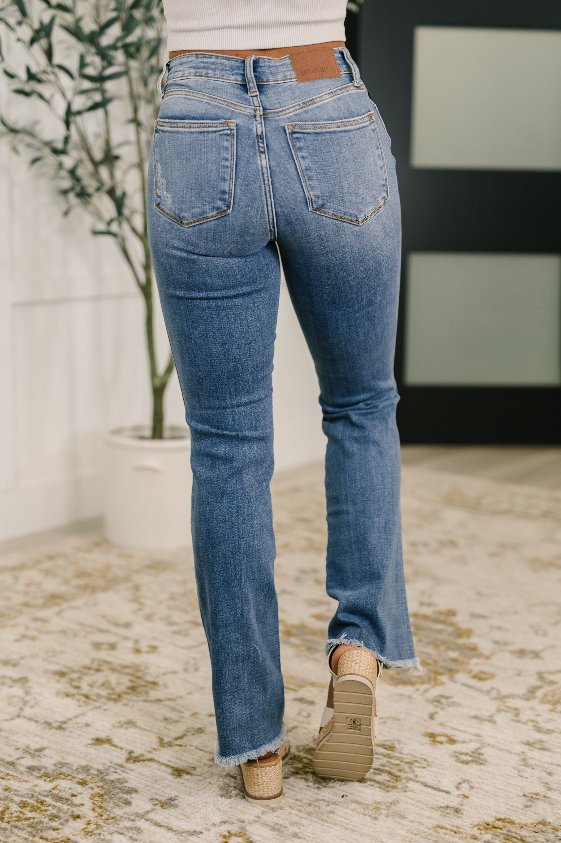 Person wearing blue jeans standing on a textured floor with a plant in the background
