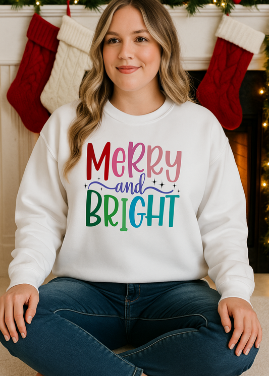 Woman wearing a white sweatshirt with 'Merry and Bright' text in colorful letters, sitting in front of a fireplace with stockings.