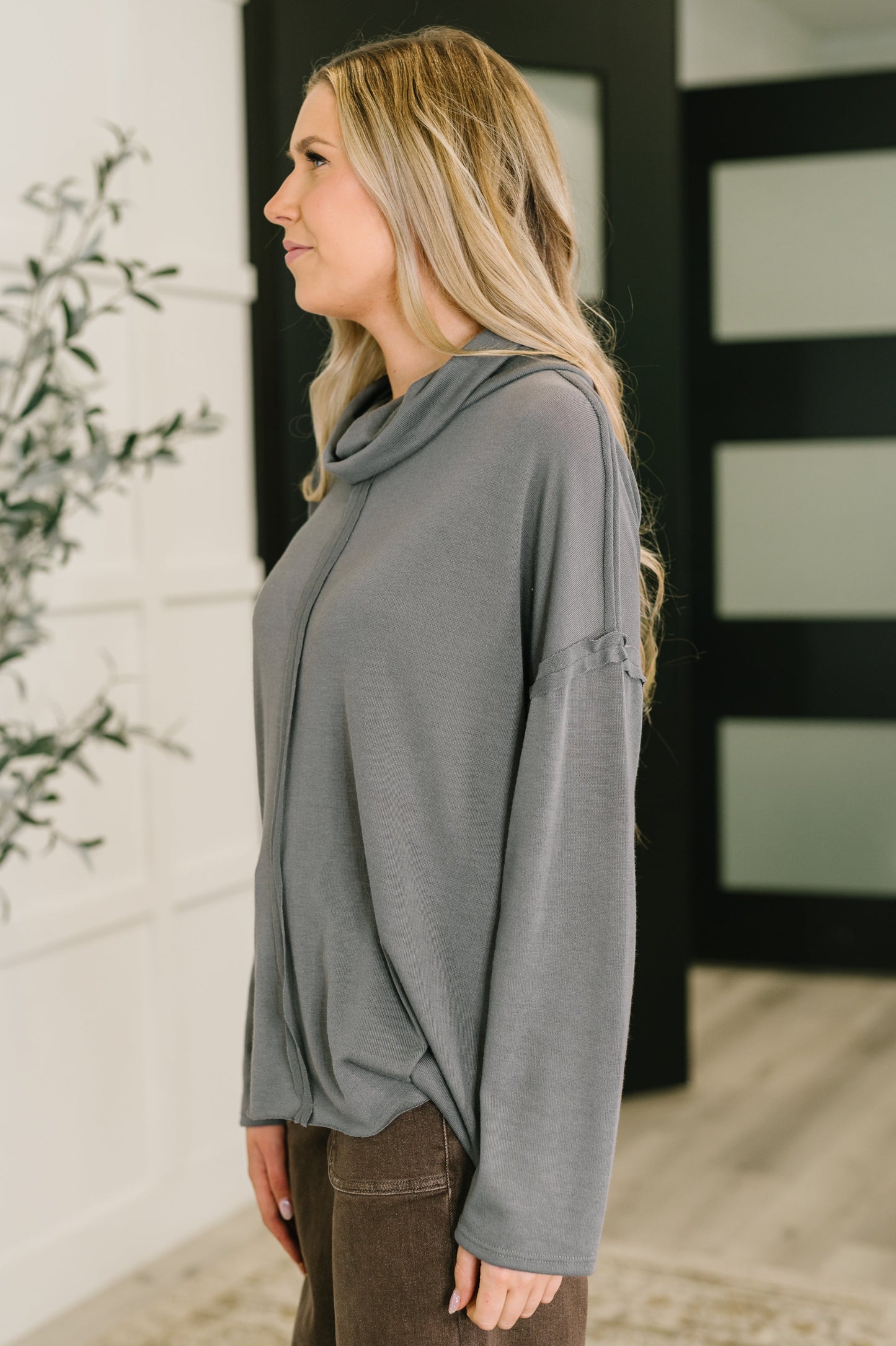 Woman wearing a gray long-sleeve top with a cowl neck, standing indoors.