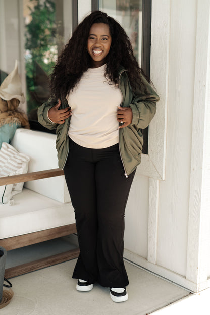 Woman standing outdoors, wearing a green jacket over a white shirt and black pants.