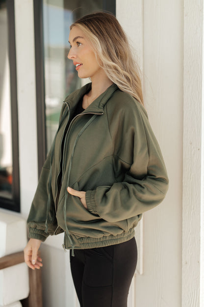 Woman wearing an olive green jacket standing indoors.