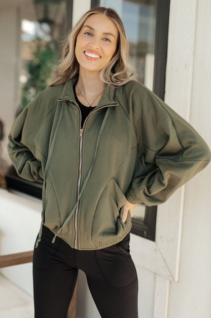 Woman wearing an olive green jacket standing indoors.