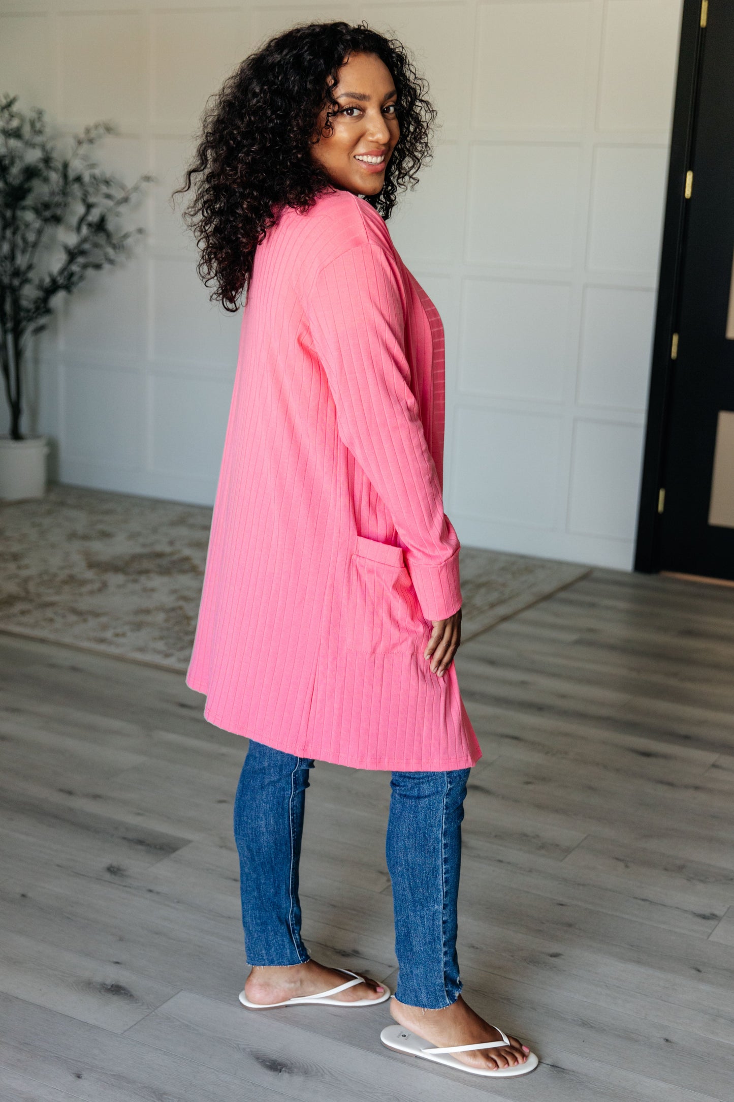 Woman wearing a pink coat and blue jeans indoors.