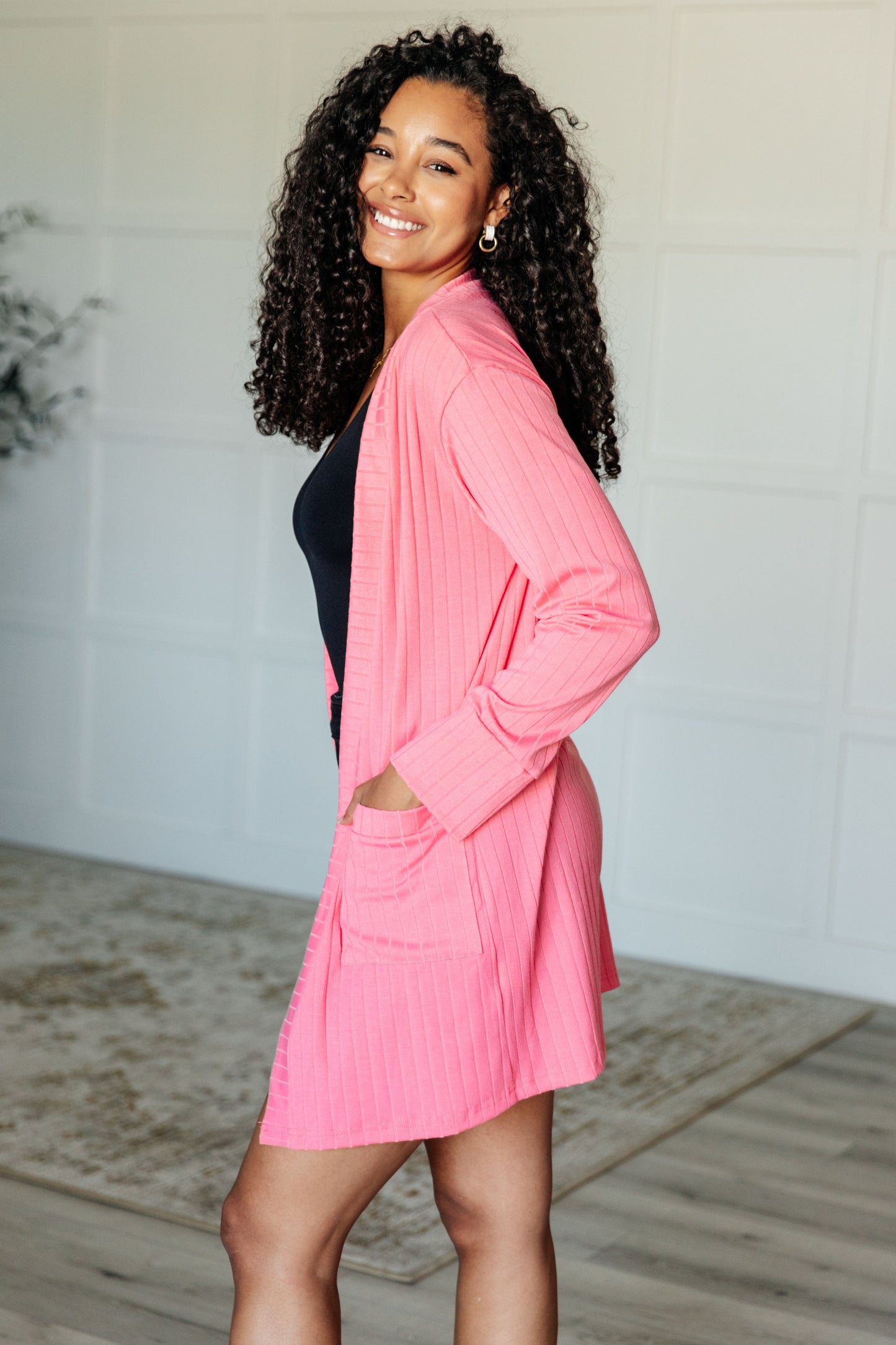 Woman wearing a pink cardigan over a black top in a minimal indoor setting