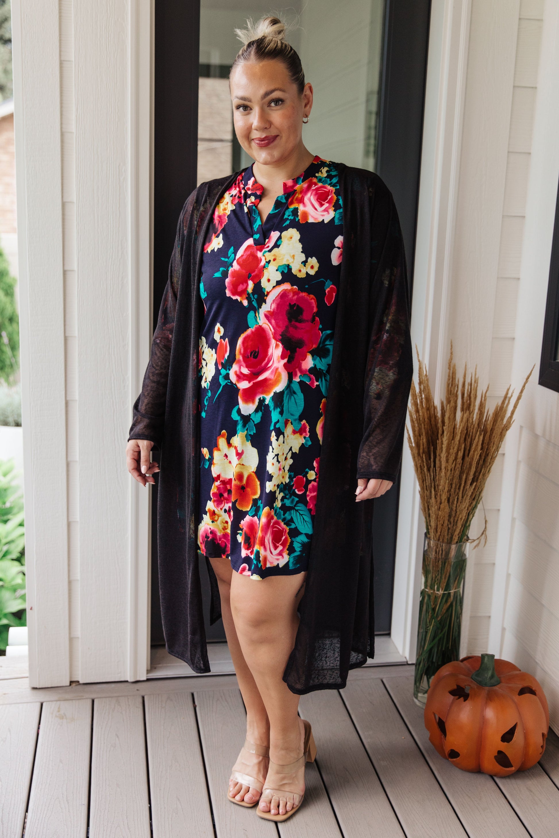 Woman wearing a floral dress with a black cardigan on a wooden deck.