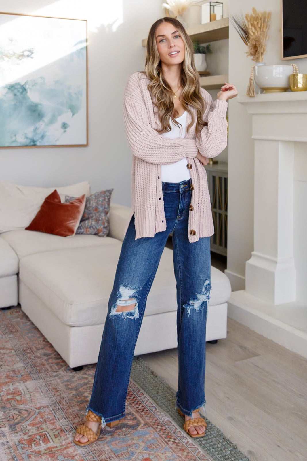 Woman in a living room wearing a pink cardigan and blue jeans.