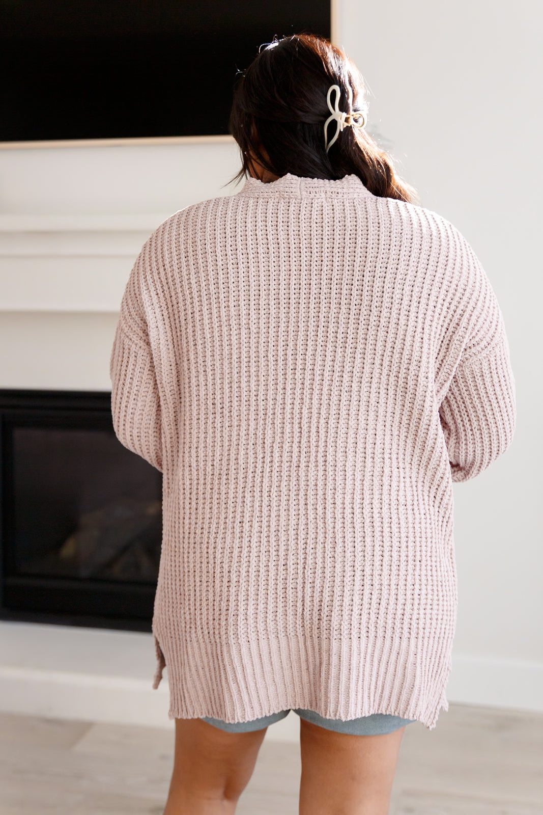 Person wearing a pink knitted cardigan in a room with a fireplace.