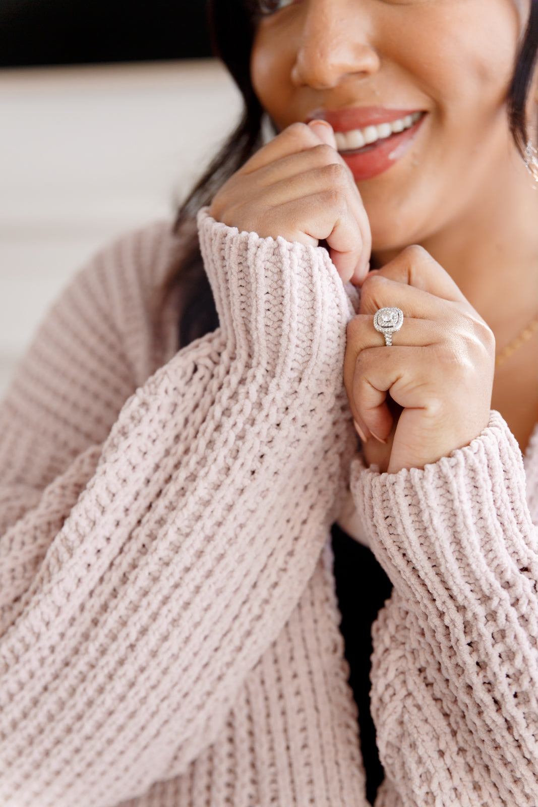 Woman wearing a pink sweater with a close-up of her hands and ring.