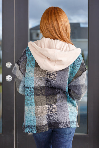 Person wearing a plaid jacket with a hood, standing in front of a glass door.