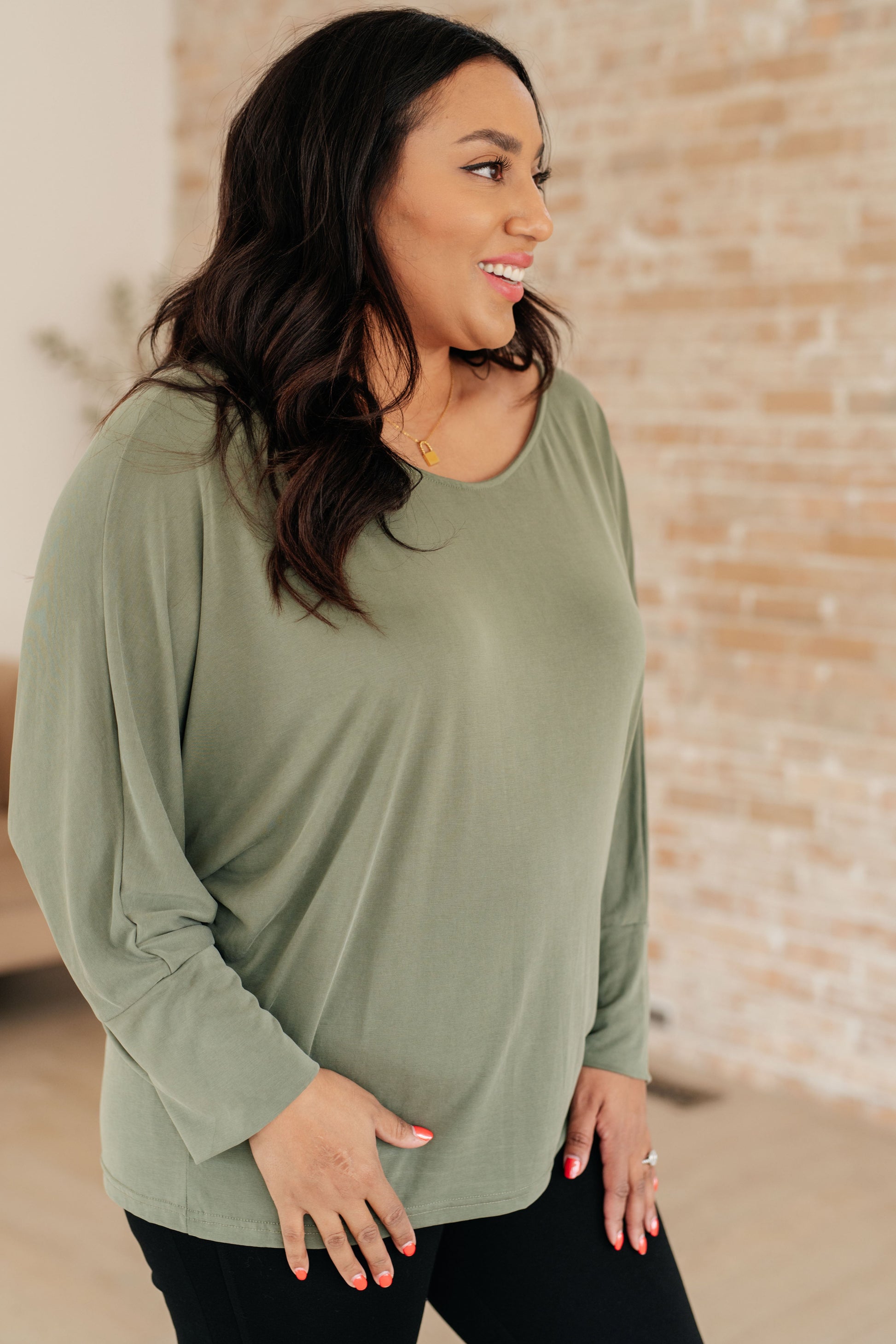 Woman wearing a green long-sleeve top with a brick wall background