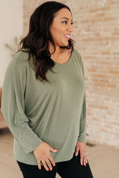 Woman wearing a green long-sleeve top with a brick wall background