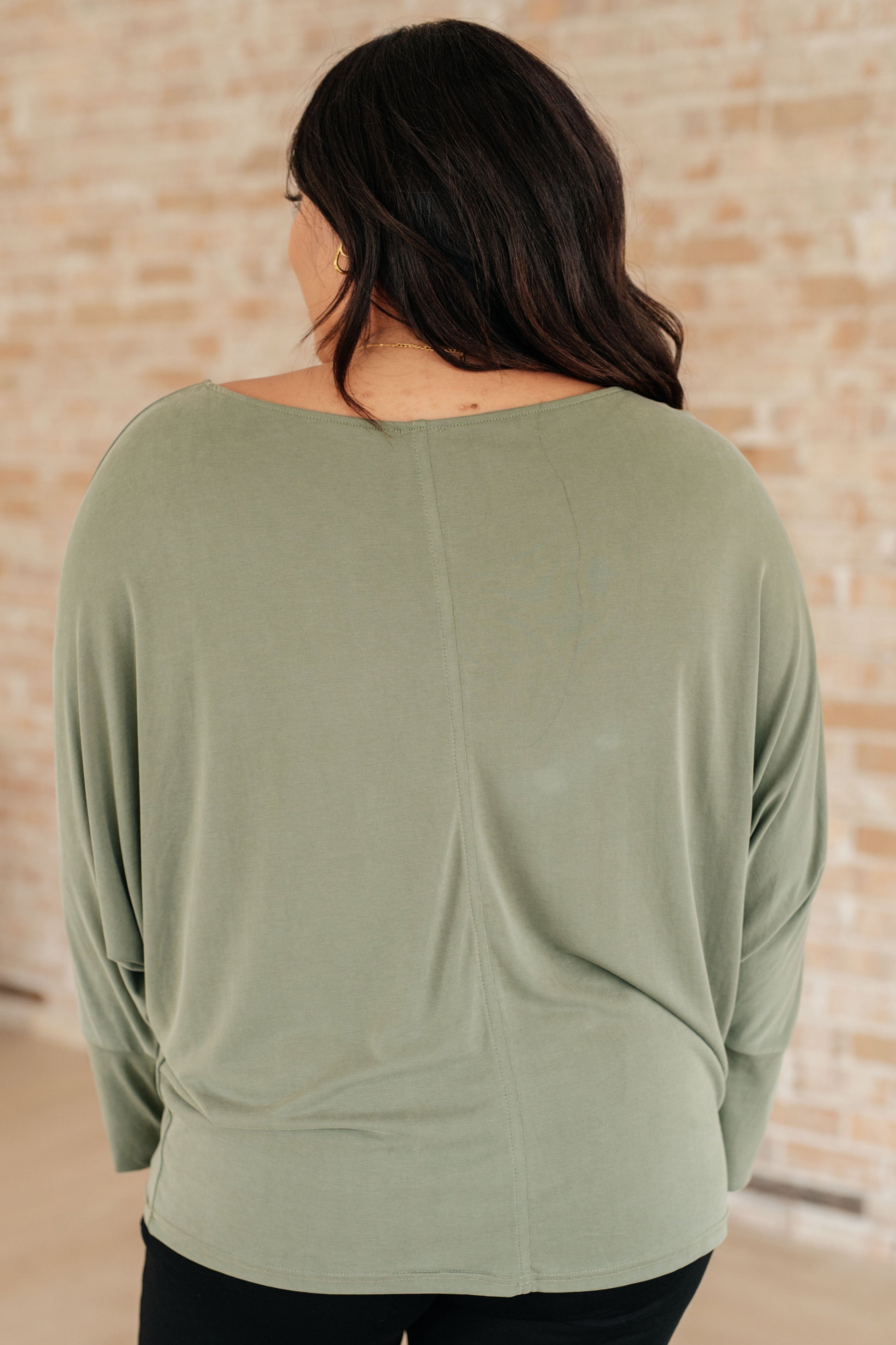 Person wearing a green long-sleeve top against a beige brick wall.