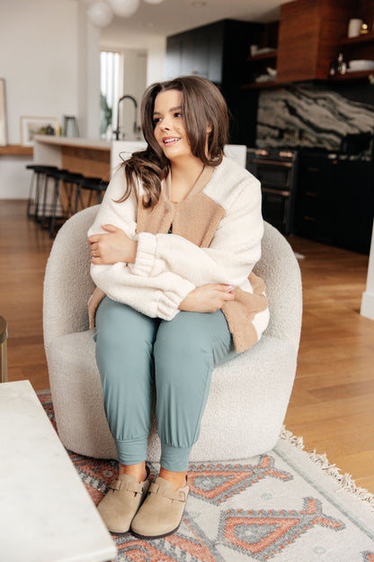 Woman sitting on a chair in a home setting, wearing a white sweater and blue pants.