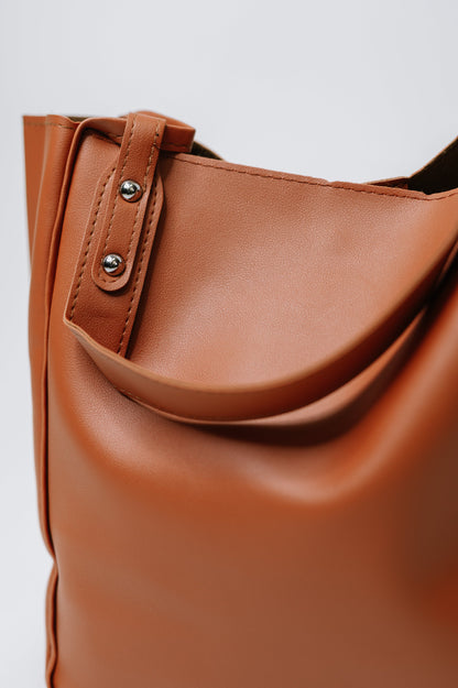 Close-up of a brown leather bag with a strap on a light gray background