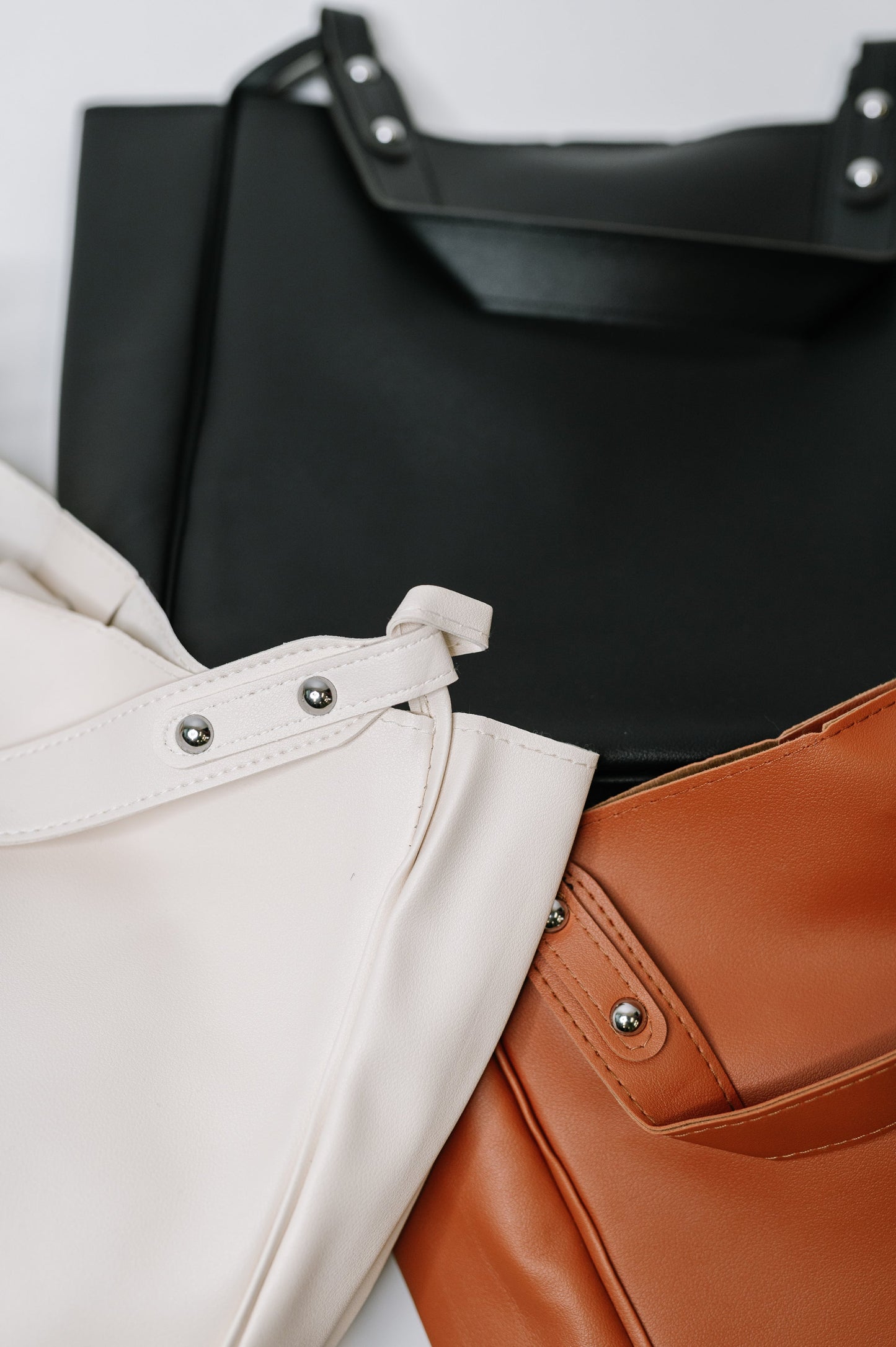 Three leather bags in black, beige, and brown on a light gray background