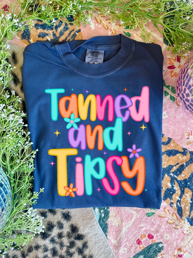 Blue sweatshirt with colorful 'Tanned and Tipsy' text on a patterned background