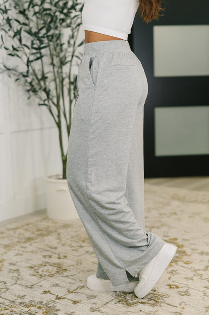 Person wearing gray sweatpants and white sneakers in a room with a plant and rug.