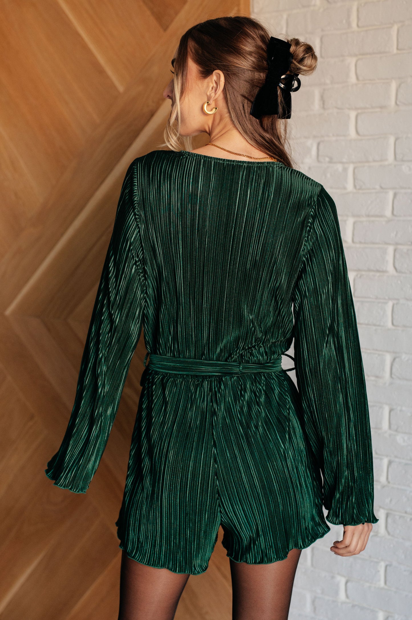 Woman wearing a green pleated dress against a white brick wall.