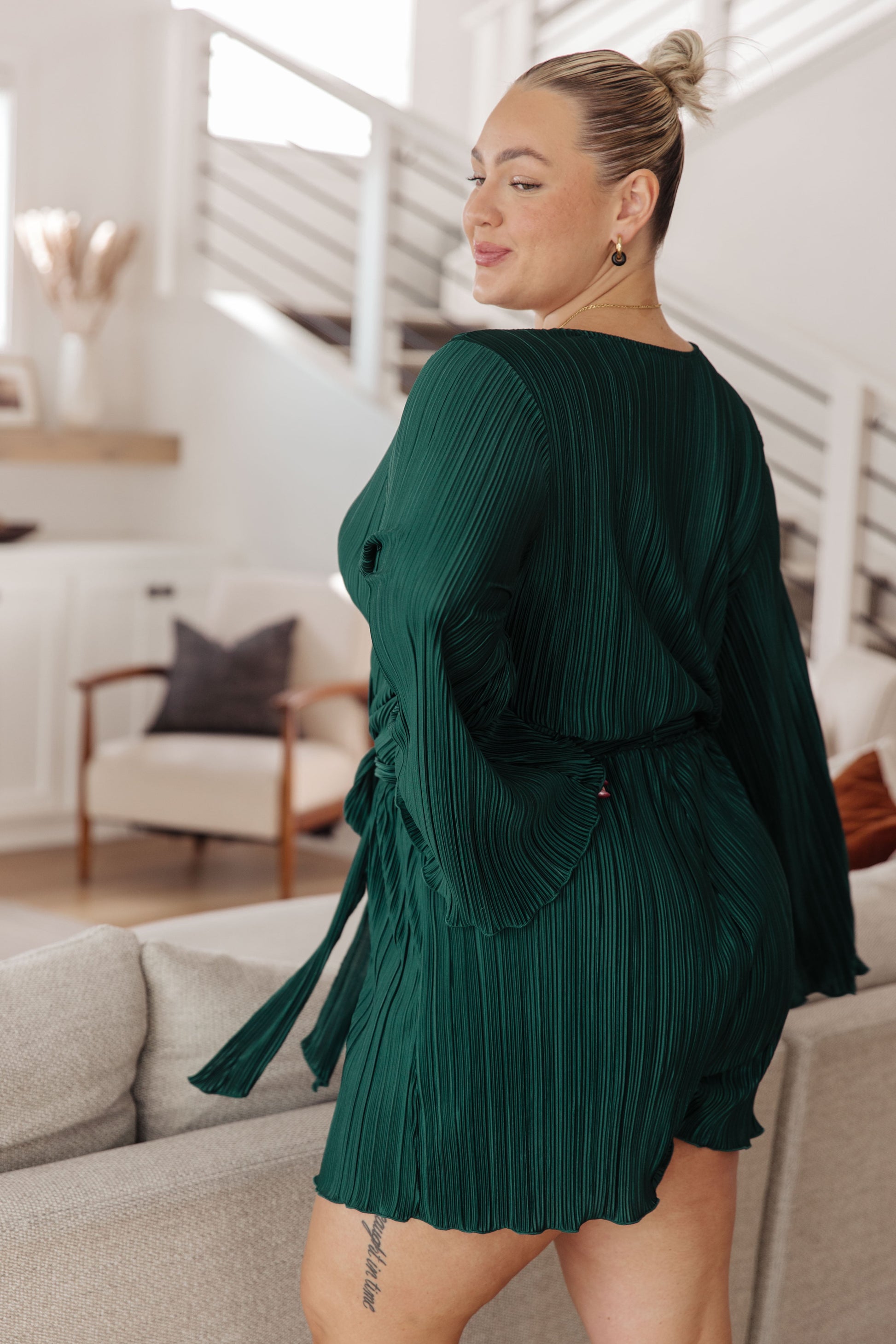 Woman wearing a green pleated dress in a living room setting