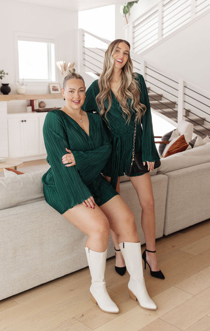 Two women in matching green outfits sitting on a couch in a living room.
