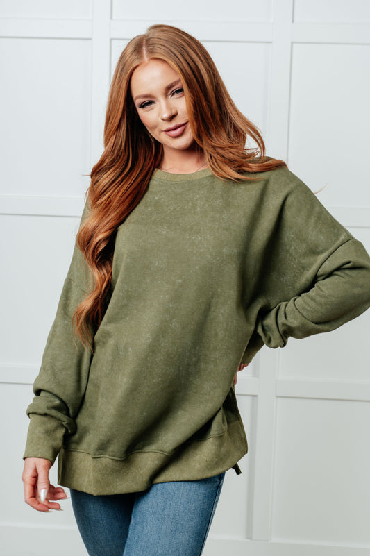 Woman wearing an olive green sweatshirt against a white wall
