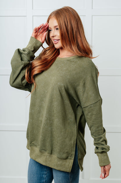 Woman wearing an olive green sweatshirt against a white wall