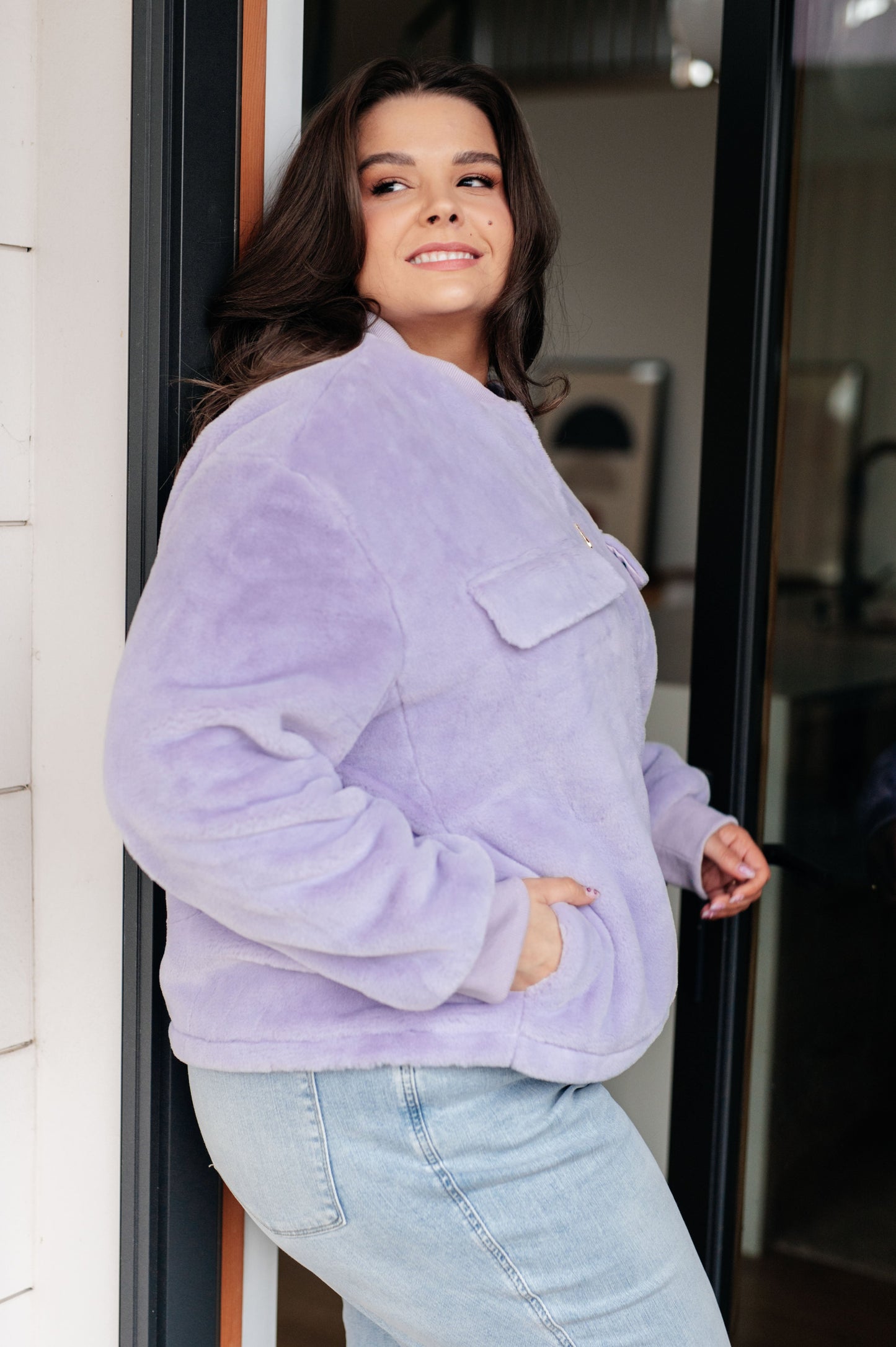 Woman wearing a light purple fleece jacket and light blue jeans standing indoors.