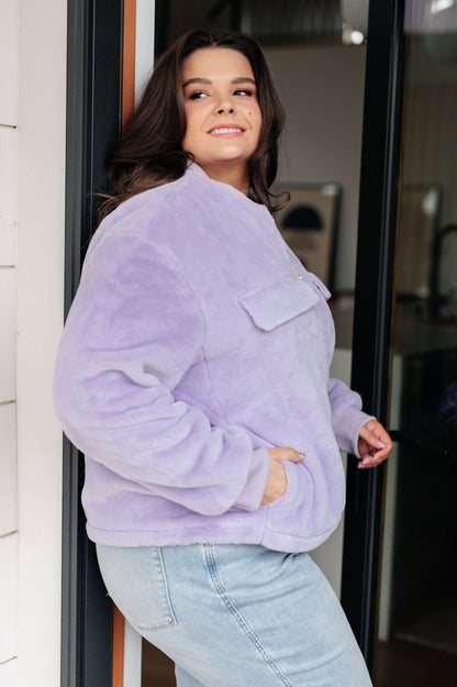Woman wearing a light purple fleece jacket and light blue jeans standing indoors.