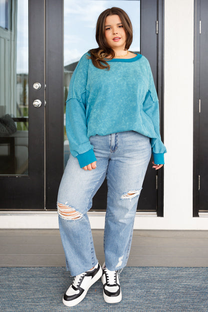 Woman wearing a blue sweater and ripped jeans standing in front of a glass door.