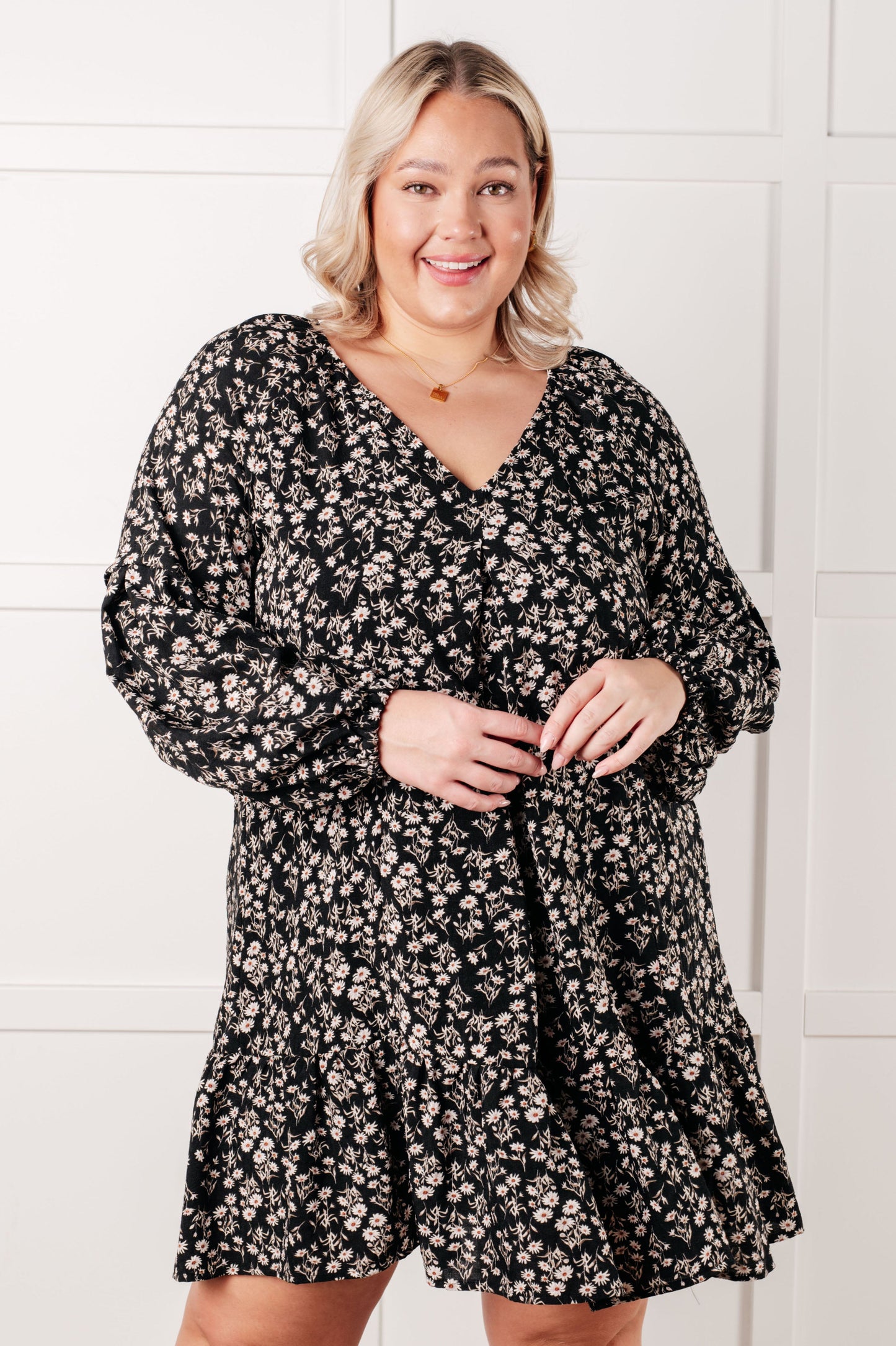 Woman wearing a black floral dress against a white tiled wall