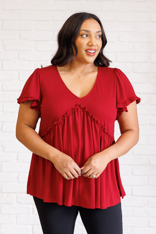 Woman wearing a red blouse with ruffled details against a white brick wall.
